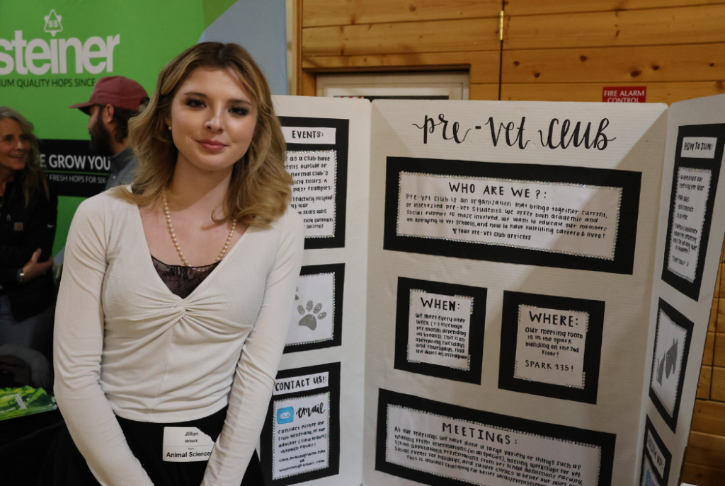 A Pre-vet club representative stands in front of a posterboard about the club, ready to chat with folks about it at the fair.