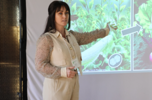 Camille Wagstaff presents in front of her slide with her arm gesturing towards her plant graphics.