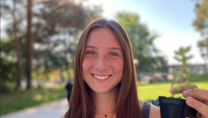 A smiling attendee of the CAHNRS Fall Festival holds up a plant proudly with the temperate fall sun glowing through the trees behind her.