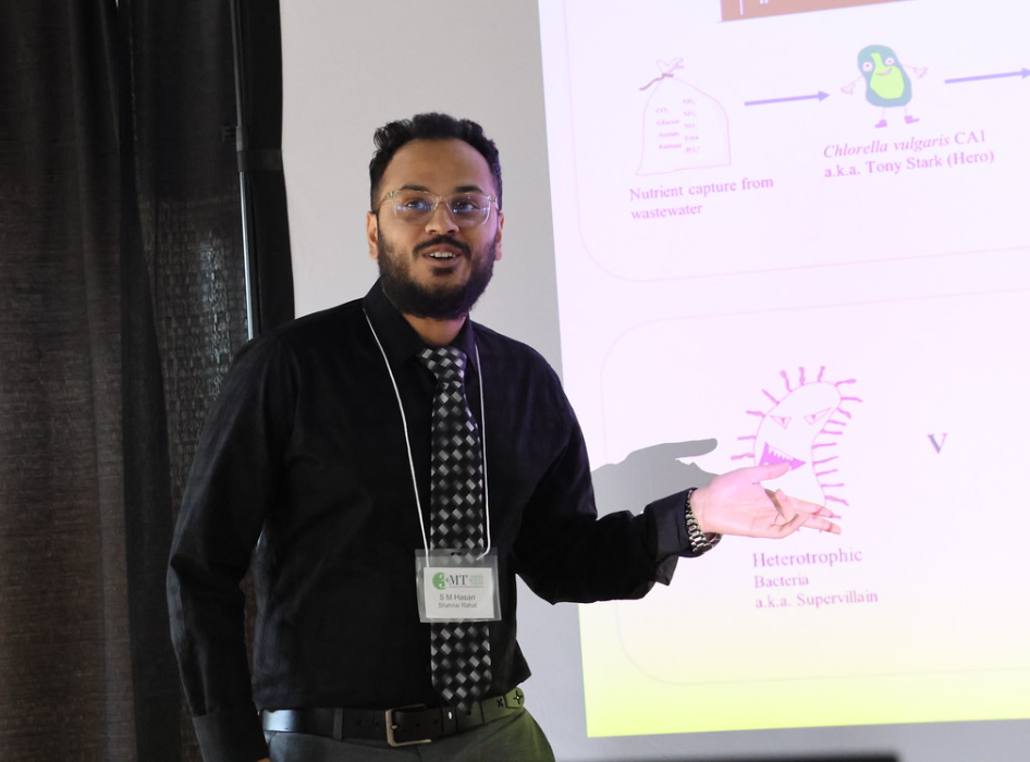 A student, one of the winners of the 3-Minute Thesis competition, stands in front of his presentation.