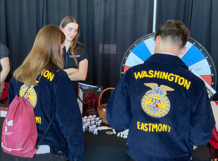 Two FFA students go to spin a wheel for a chance to win prizes, such as a tiny stress-ball squishy cow keychain, at the WSU FFA convention.