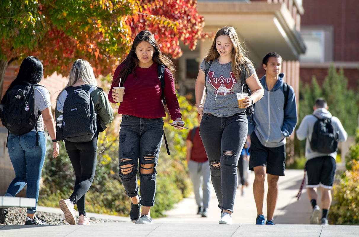 Two students in WSU themed outfits, chat on their way to class with their iced coffees in hand.