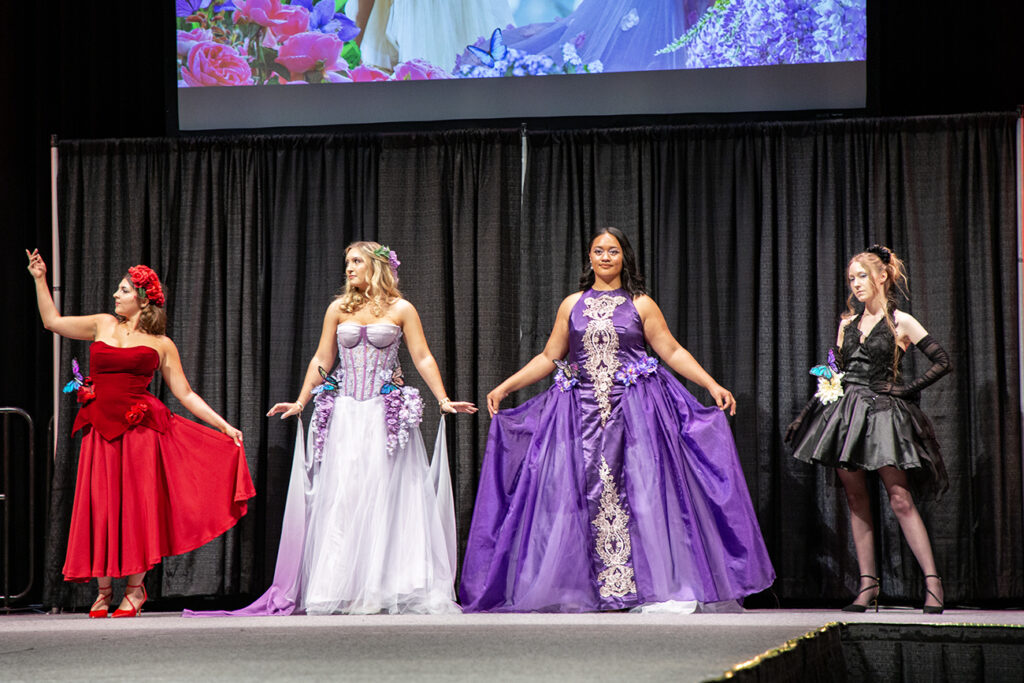 Four models in majestic floral gowns pose at the end of the runway.
