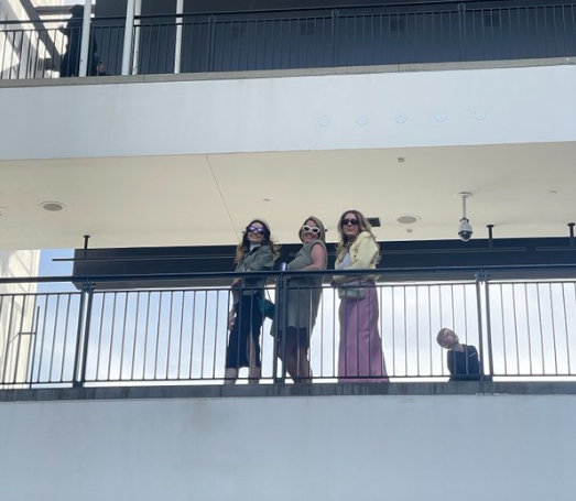 Three AMDT trip attendees look down from a high-up balcony with sunglasses.