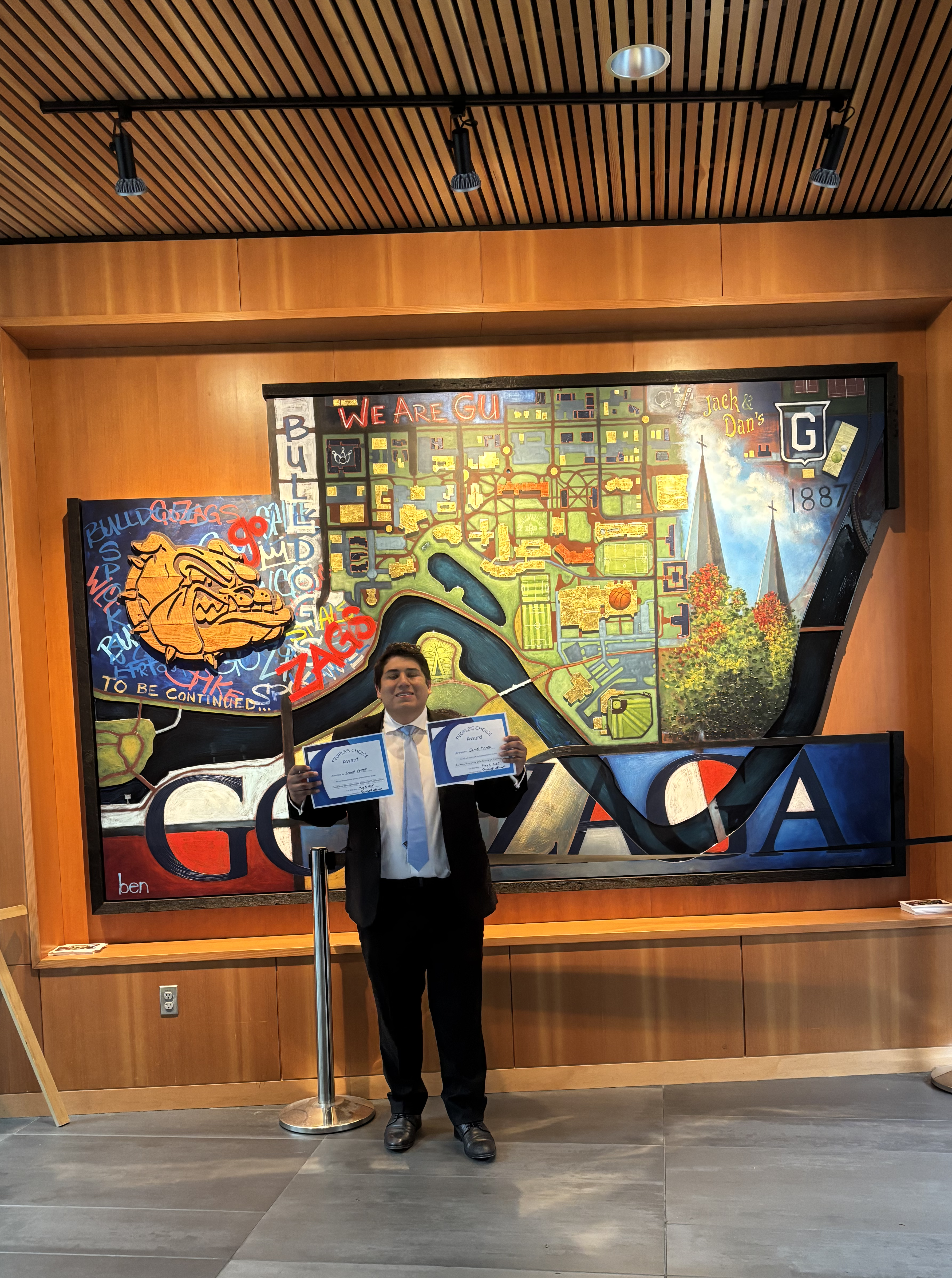 Daniel Arinez poses with his two People's Choice awards in front of an art wall at Gonzaga University.