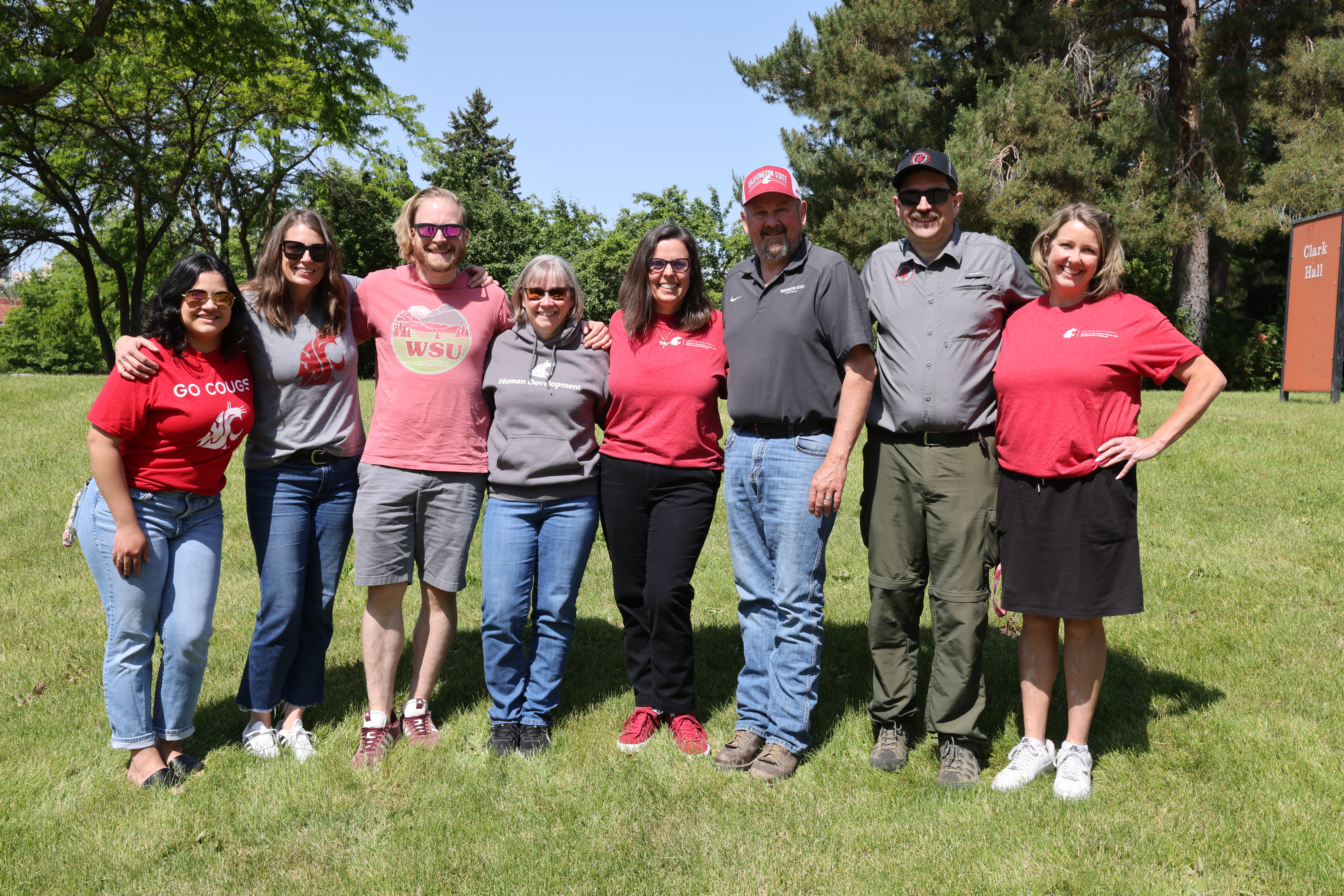 8 CAHNRS Advisors stand with shoulders linked in the grass outdoors.