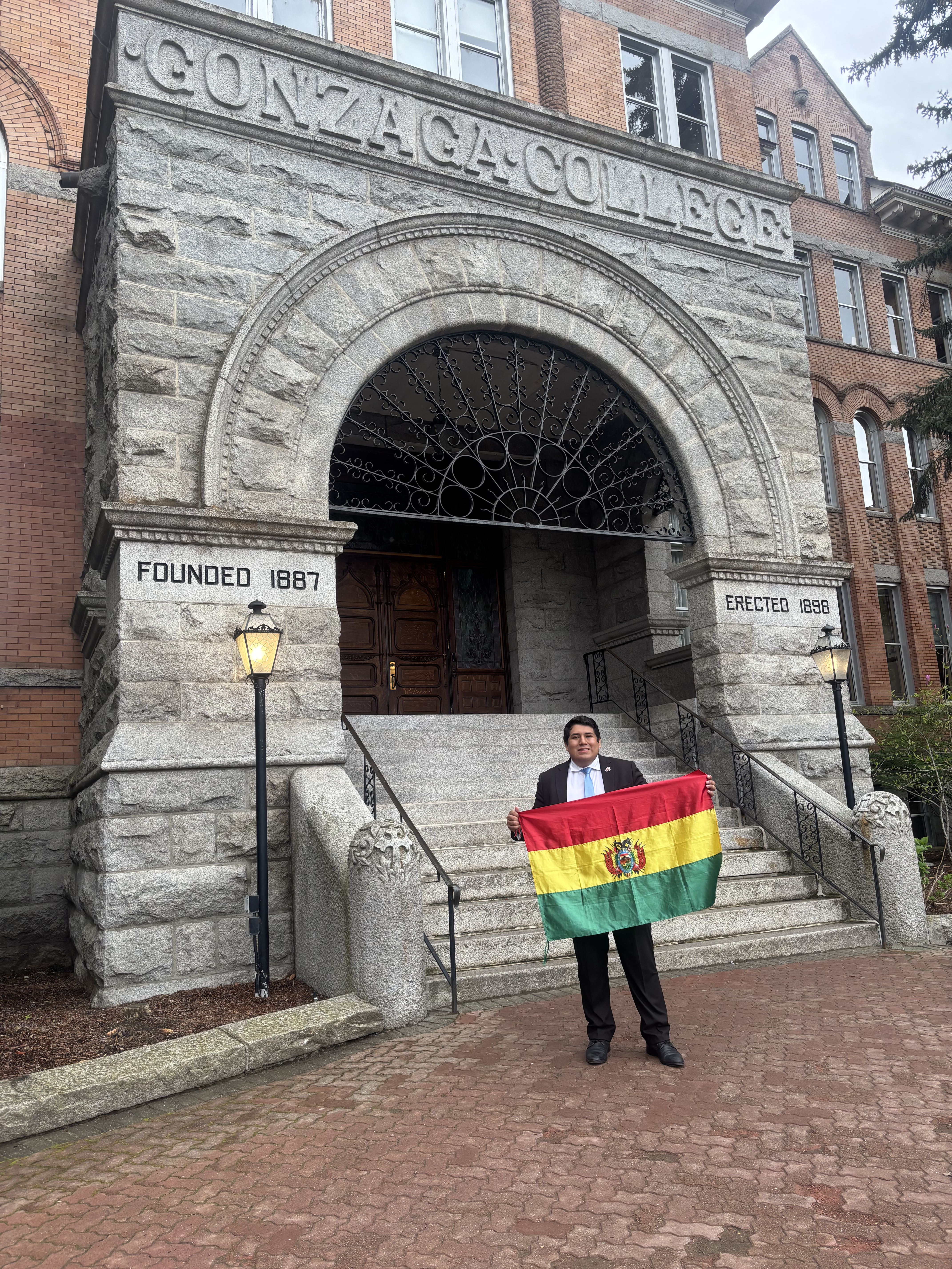 Daniel Arinez poses with the Bolivian flag, his home country's flag, in front of an archway at a historical building built in 1898 at Gonzaga University.