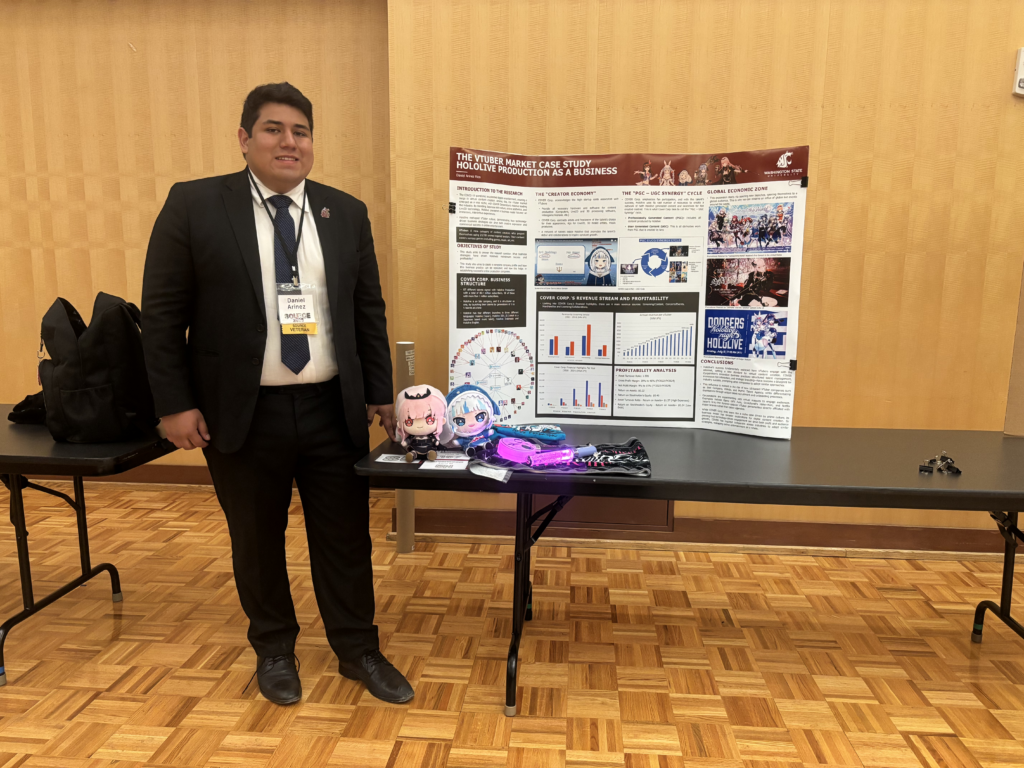 Daniel Arinez poses with anime-style character plushies alongside his research paper board. It features text, graphs, and the title The VTuber Market Case Study: Hololive Production as a Business.