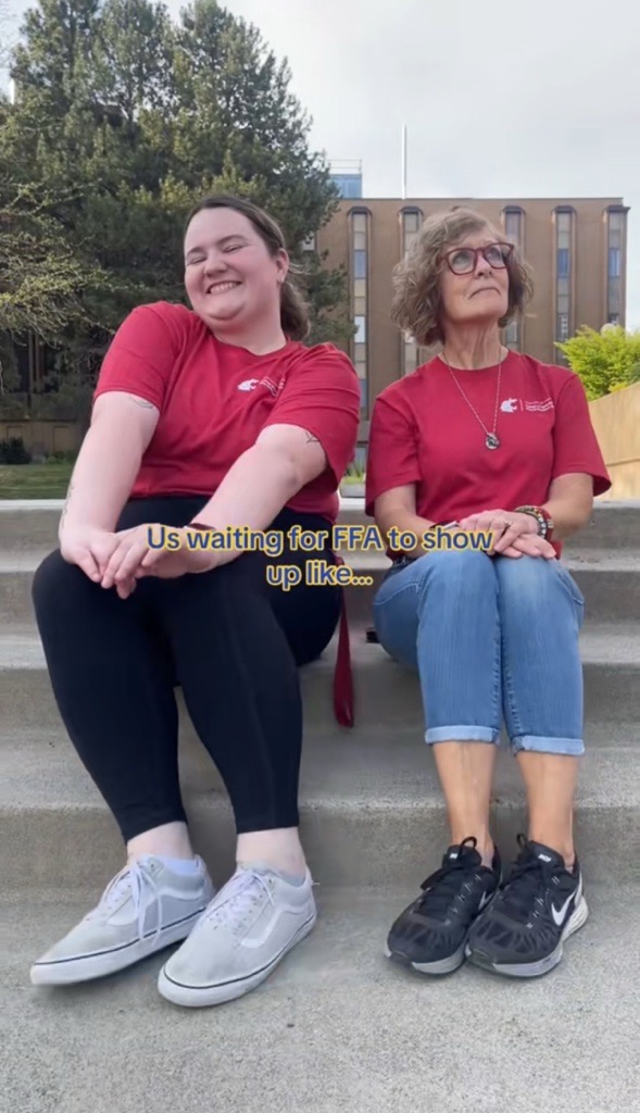 Emily Libey looks so excited, while Judy Hopkins stares off with a look of wondering on her face. Both are dancing with their feet, sitting on the steps of Spillman Plaza. The text in the middle reads "Us waiting for FFA to show up like..."