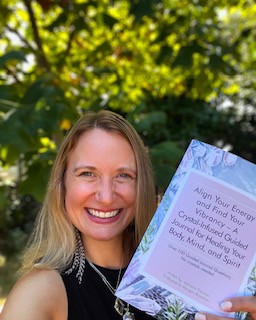 Adriana Thomas holds up a book called "Align Your Energy and Find Your Vibrance - a Crystal-Infused Guided Journal for Healing Your Body, Mind, and Spirit.