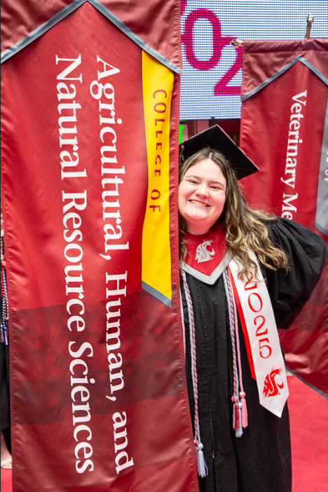 Emily Libey holding the CAHNRS gonfalon in her grad cap and gown.
