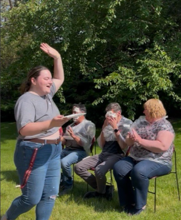 Emily Libey with her hand in the air in triumph while Scot tries to wipe the whipped cream out of his eyes.