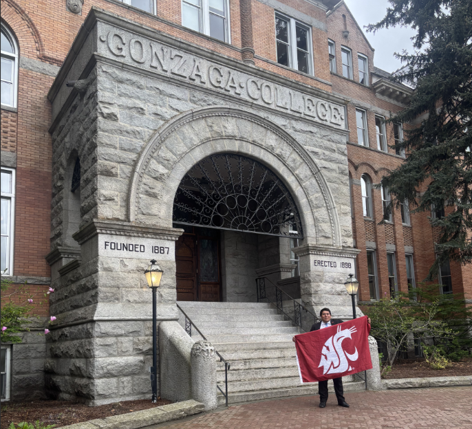 Daniel Arinez holding the Coug flag in front of an archway of a historical building built in 1898 at Gonzaga University.