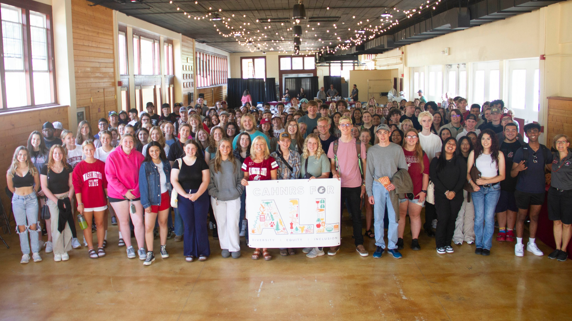 Hundreds of students surround Nancy Deringer, helping hold the CAHNRS For All banner.