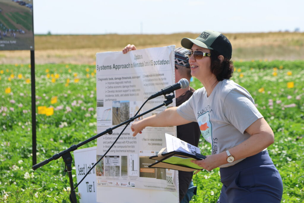 A speaker presents with a posterboard with graphs on the topic of a Systems Approach for potatoes.