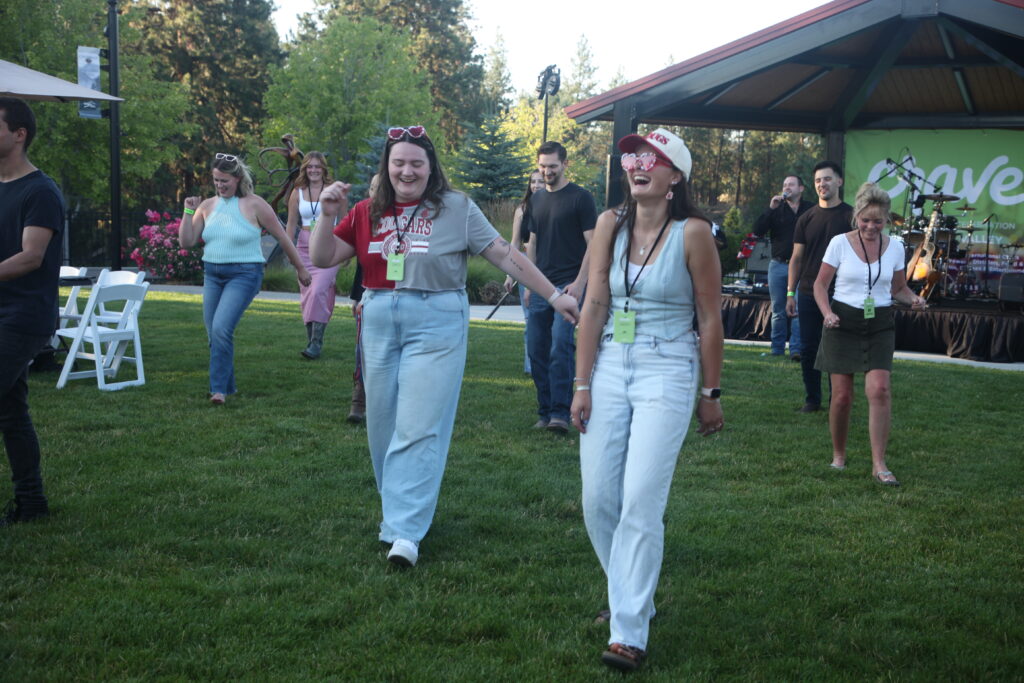 A group of festival goers line dance in front of the live music band.