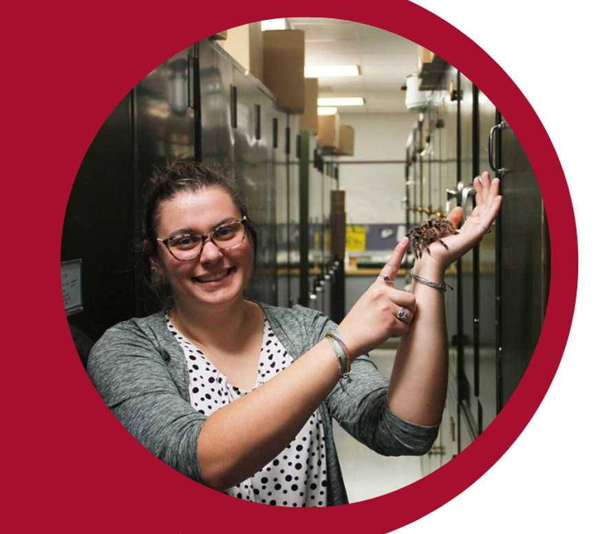 An Entomology representative holds a large furry tarantula in her hand, gently petting it with a huge smile on her face.
