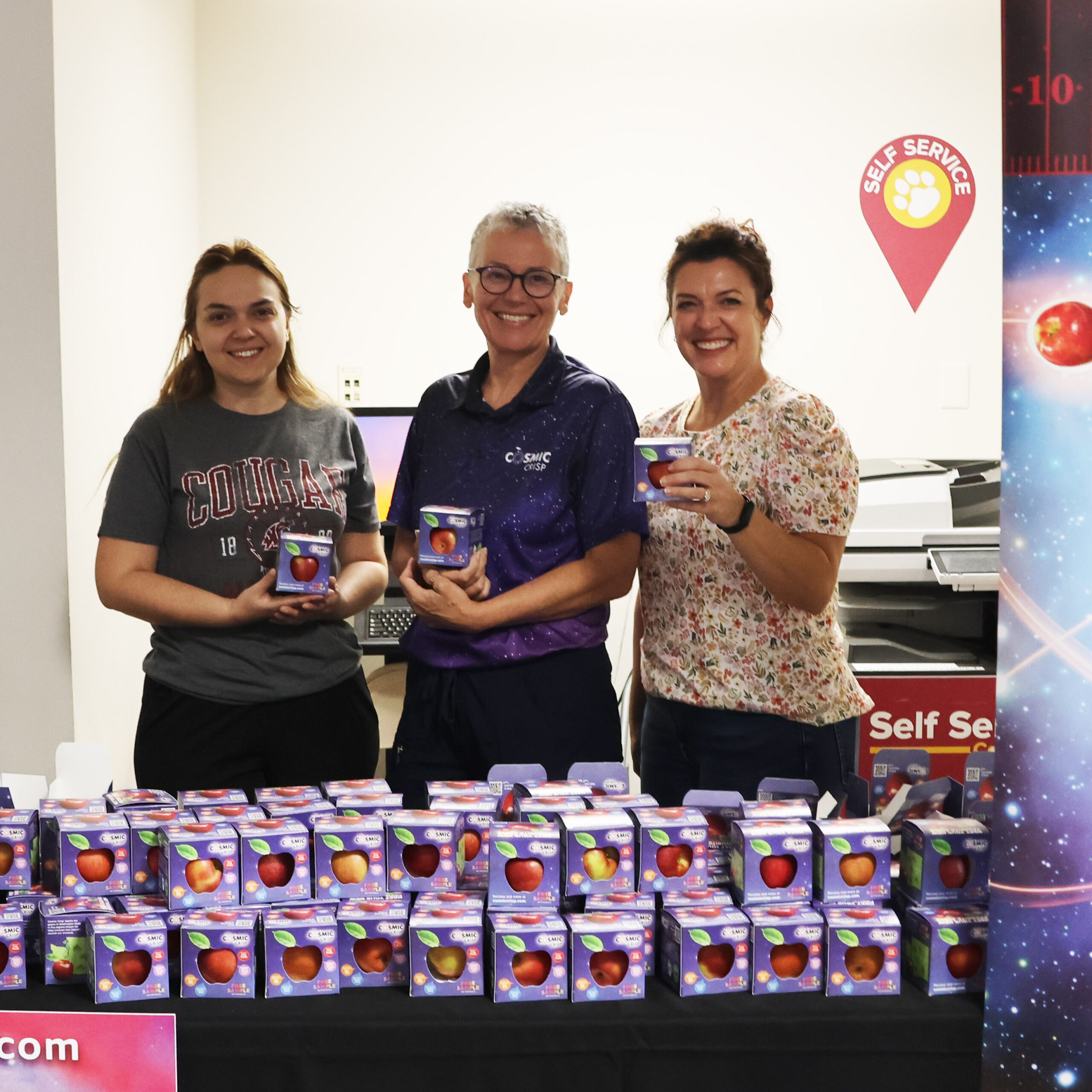 Smiling volunteers hold Cosmic Crisp boxes, ready to hand them out at move-in weekend.