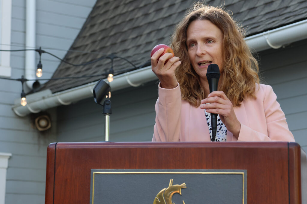 Director of the Washington Tree Fruit Research Commission (WTFRC), Ines Hanrahan, holds a Cosmic Crisp as she gives her talk at the Alumni Centre.