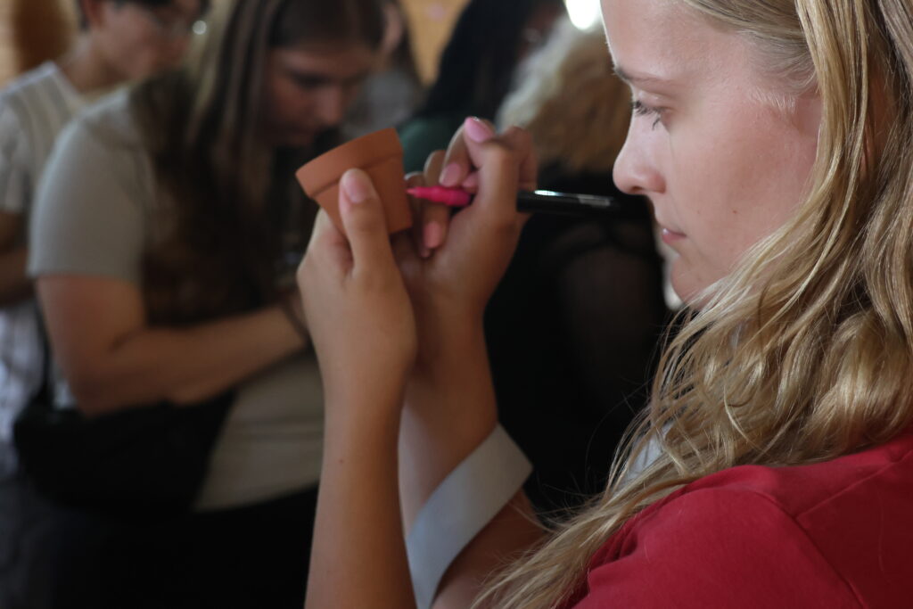 A student draws her name on her mini plant pot before planting it.