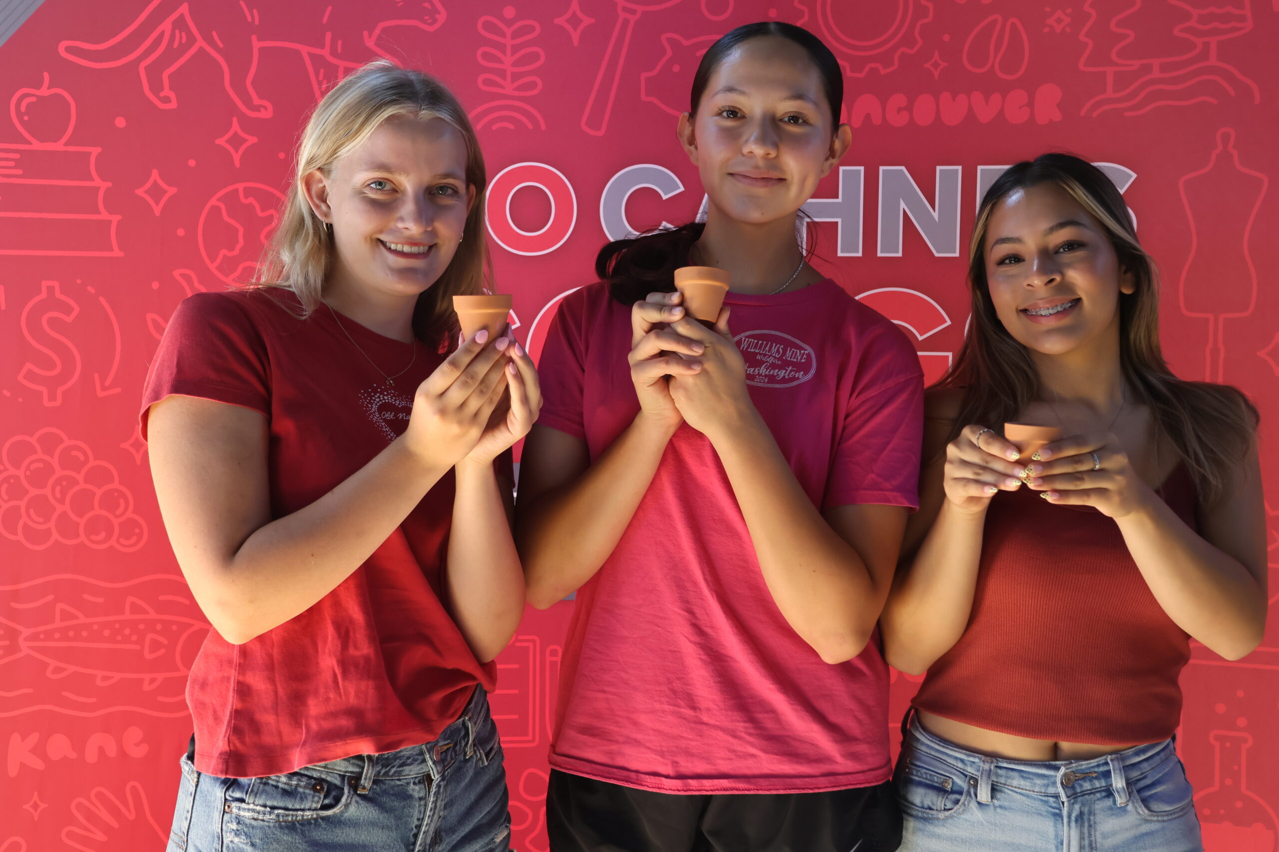 Three students hold up their potted mini plants