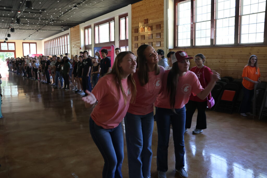 Three students pose at the beginning of a double-line of students in Ensminger Pavilion, filming a fun TikTok video.