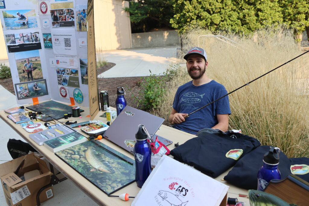 The fisheries booth features a volunteer holding a fishing rodd
