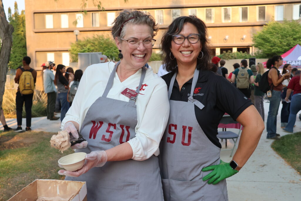 Kat Odell from CAHNRS Operations and Laura Lavine from Entomology pose in their WSU aprons while scooping ice cream