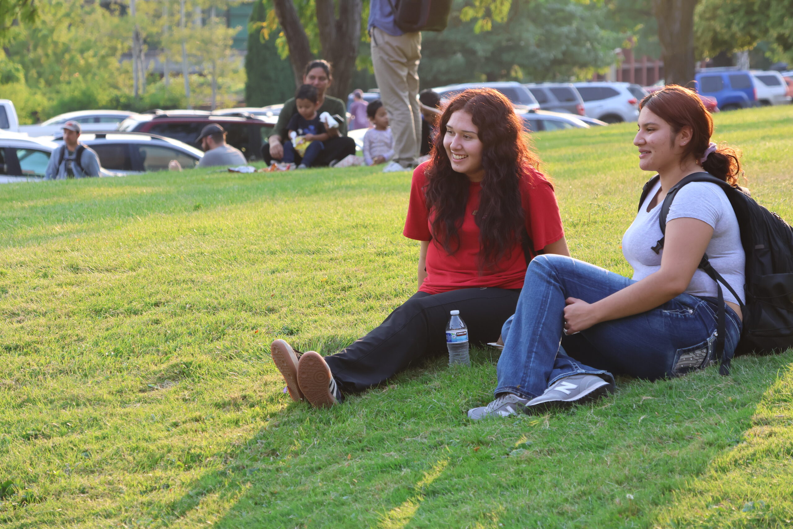 two students mingle on the grass near fall fest, with the warm late-summer sun shining down behind them.