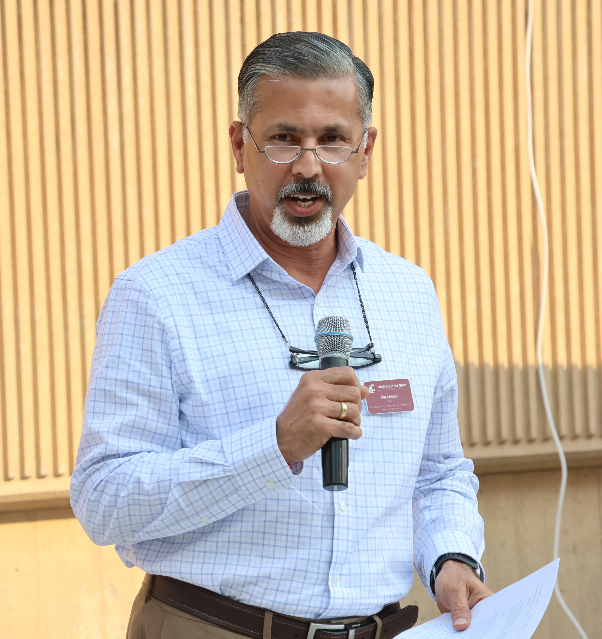 Dean Raj Khosla holds a microphone while giving a speech