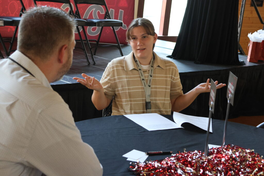 A student puts their hands up in a gesture of asking advice from a faculty mentor at Orientation Dinner for Top Scholars