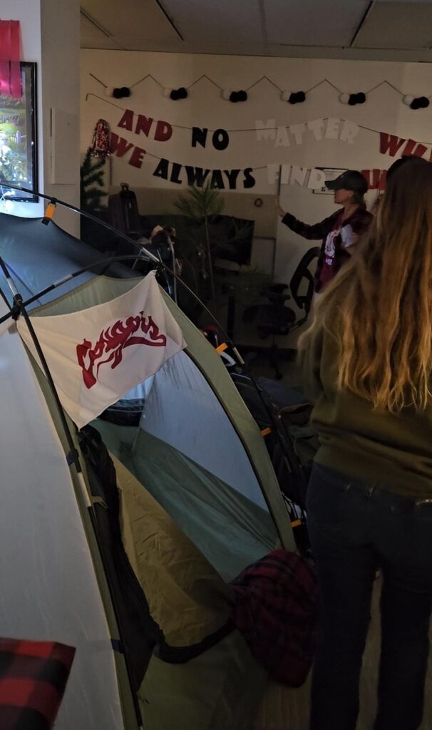 a Cougars tent is in the center of a dark, woodsy office. The words "And no matter what, we always find our way back home" are hanging on the wall behind