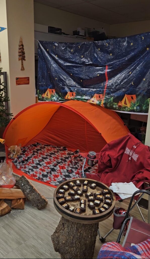 brownie s'mores are served on a log table in front of a tent and a sky background