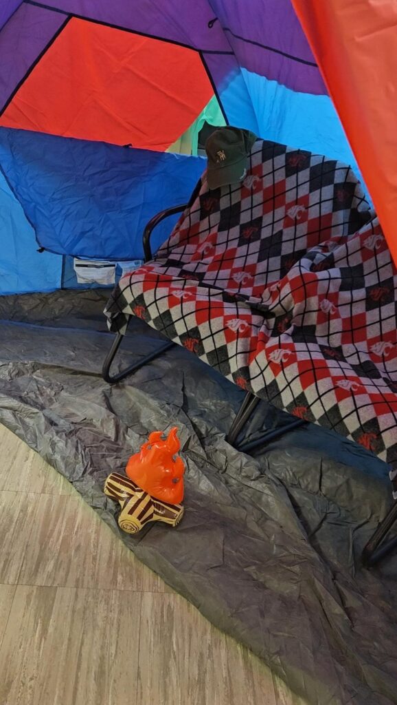 A closeup of a tent with an official argyle Cougars print blanket on a couch, with a mini fake fire