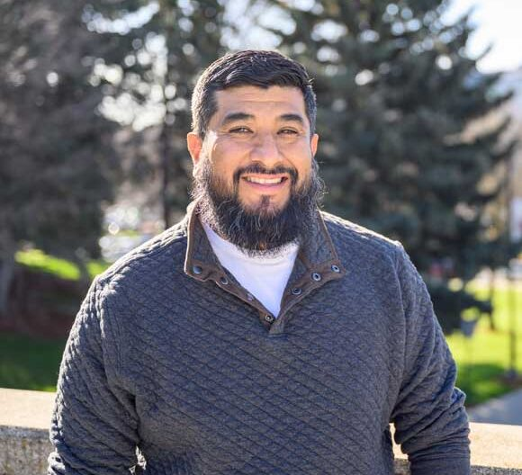 Junior Gomez presents a friendly and welcoming smile with a tree background.