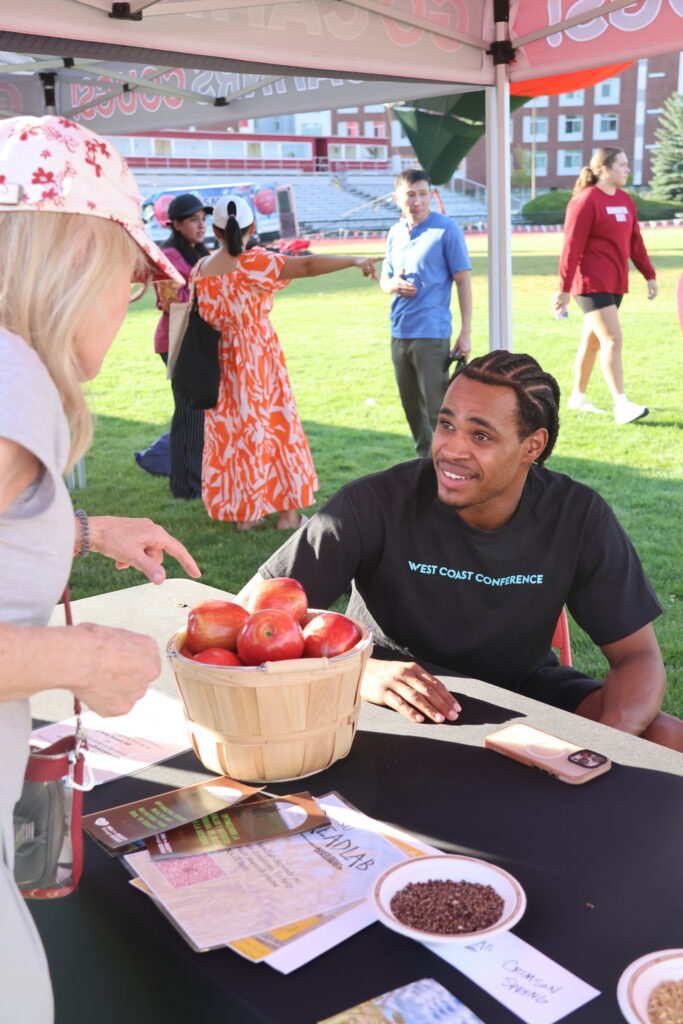 A volunteer explains the apples to an attendee at the Apple Cup tailgate