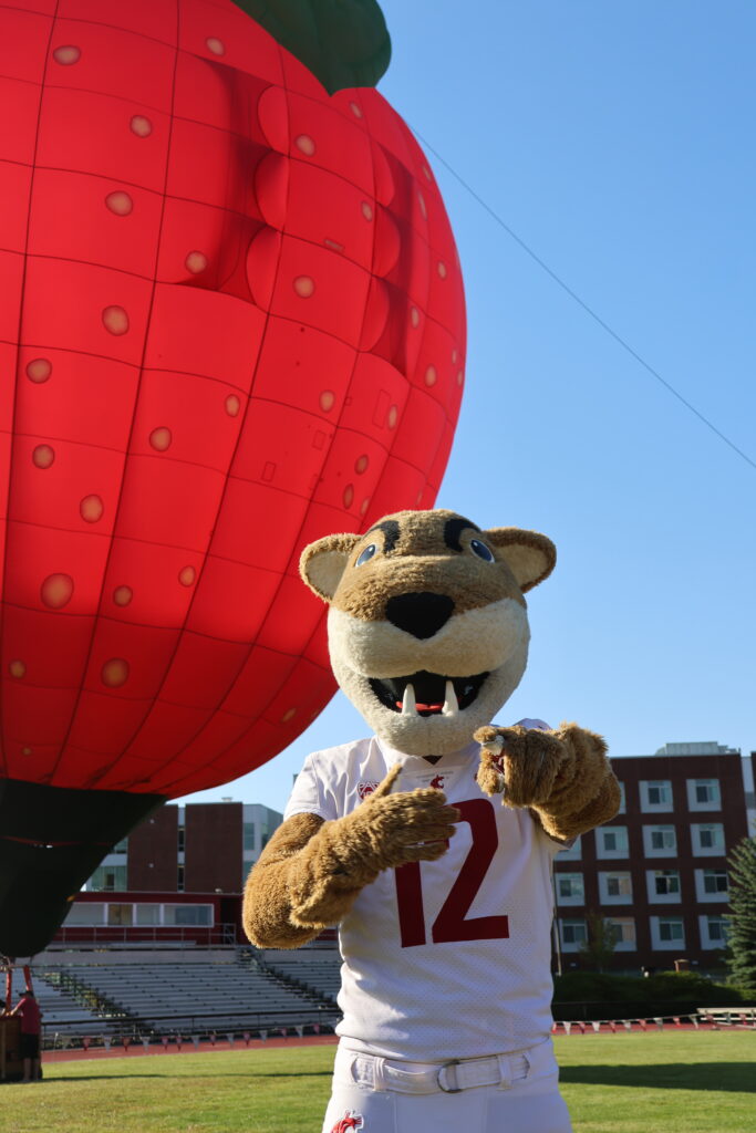 Butch points at the camera enthusiastically, the Cosmic Crisp apple-shaped balloon behind him