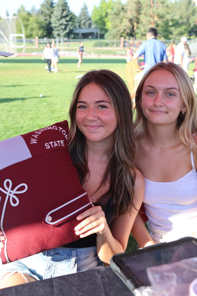 Two AMDT students hold a pillow made from recycled WSU band uniforms at a stand before the Apple Cup game