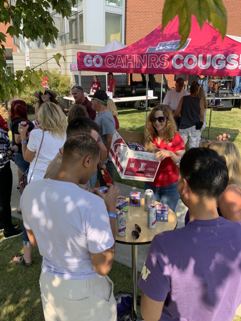 Cosmic Crisp apples are handed out at the tailgate, and guests are enjoying the shade with their beers and apples, standing at cocktail tables.