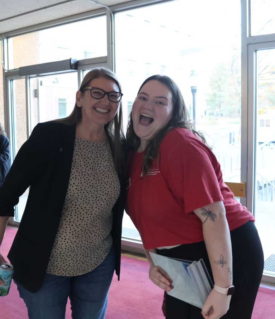 Two attendees to the All CAHNRS Meeting smile enthusiastically that they got to meet there, standing in front of the entrance to Johnson Hall with the crimson carpet. 
