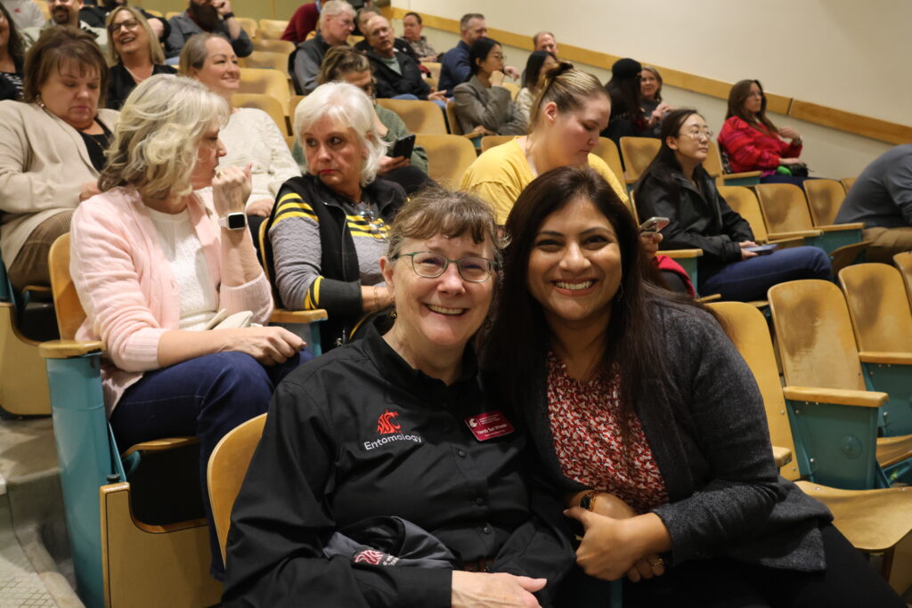 Attendees of the All CAHNRS Meeting are chatting intently and smiling as they wait for the meeting to start, sitting in rows of classroom seating.