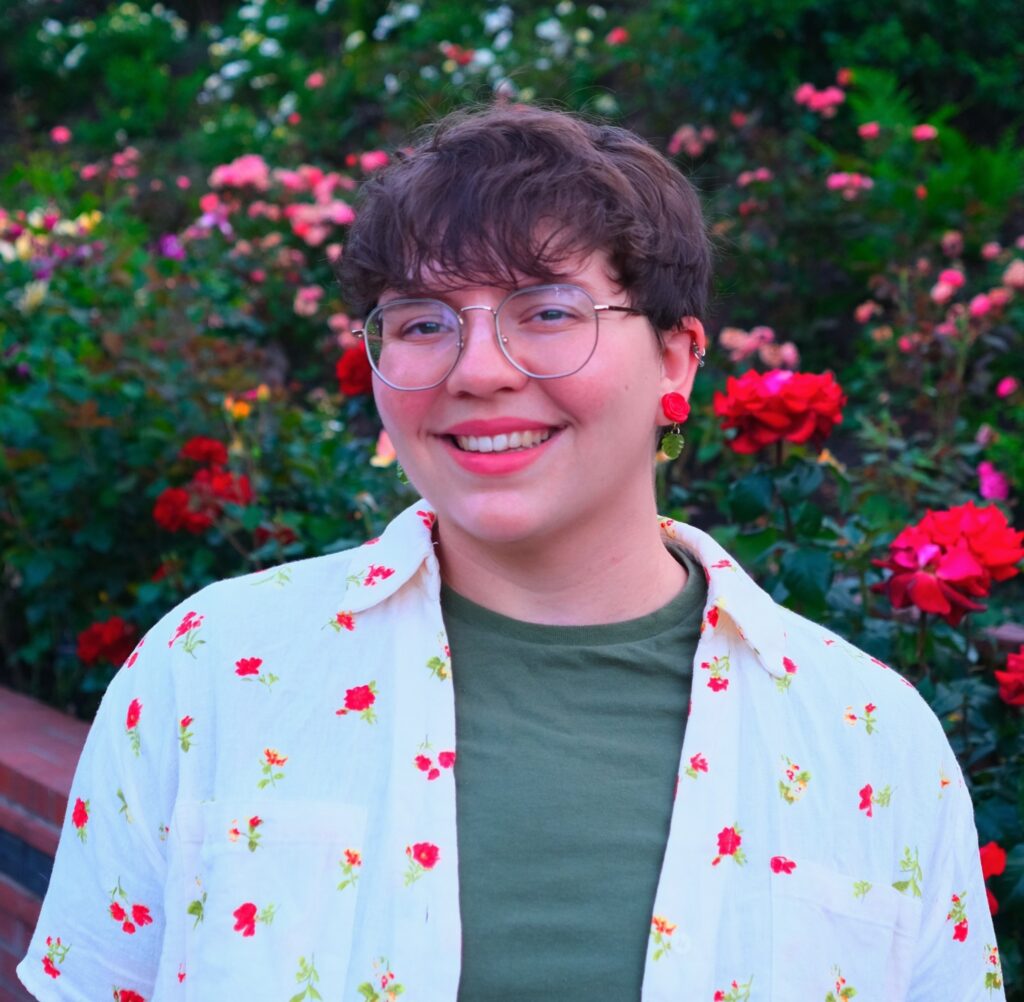 Cal Verstrate is in a garden of colorful roses wearing a fitting floral pattern on their clothes.