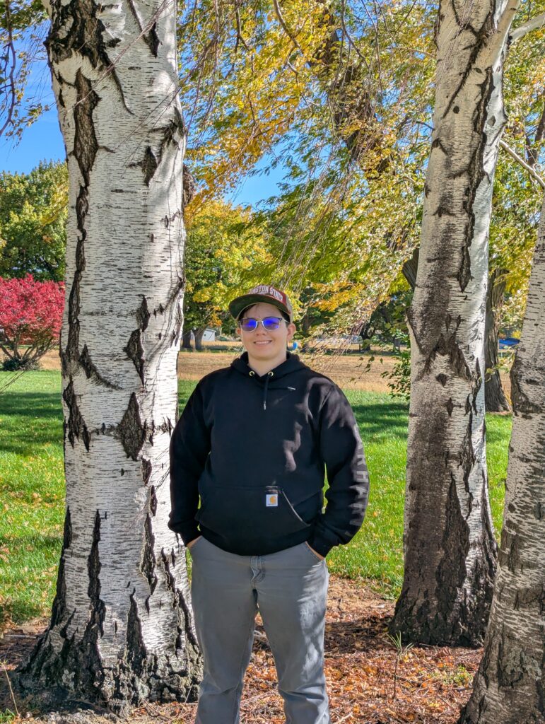 Em Rendleman wears a Washington State University hat amongst vibrant trees on a lovely outdoor adventure.