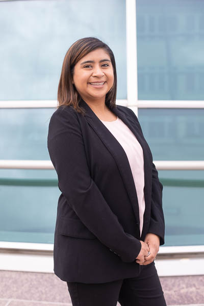 Nancy Hernandez smiles in a professional suit in front of campus windows.