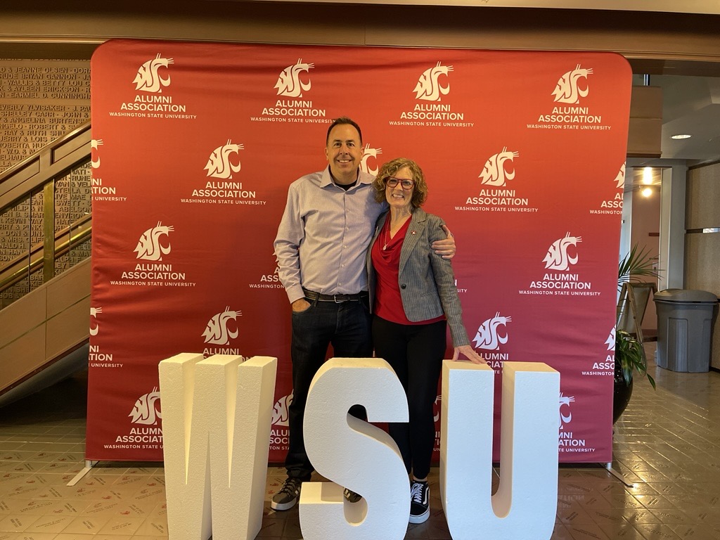 Corey Ciochetti and Judy Hopkins from CAHNRS SSAP pose together with the WSU letters sign in the Alumni Association building.