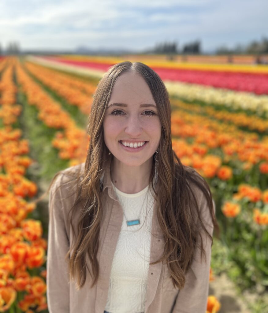 Nicole Jones smiles brightly on a sunny day in a huge field of rows and rows of flowers.