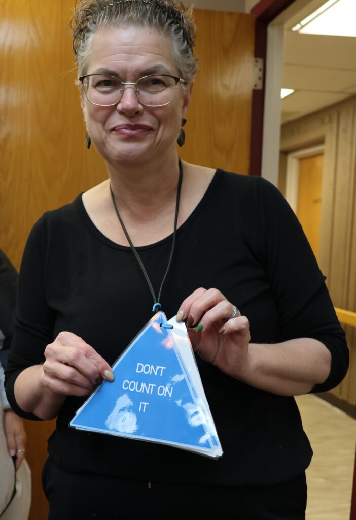 Kat Odell looks smug while holding a triangle necklace card that says "Don't Count on It". 