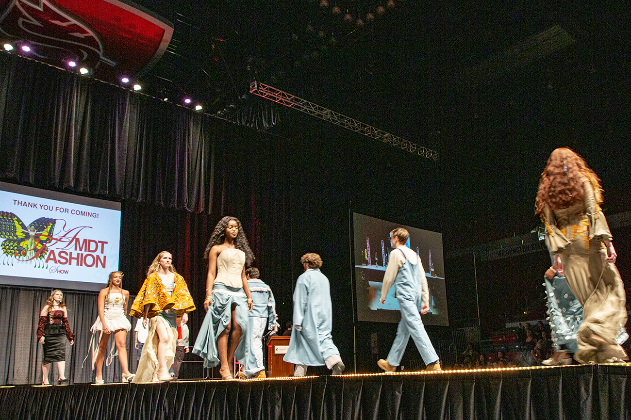 College students walking a catwalk while wearing garments made by designers.