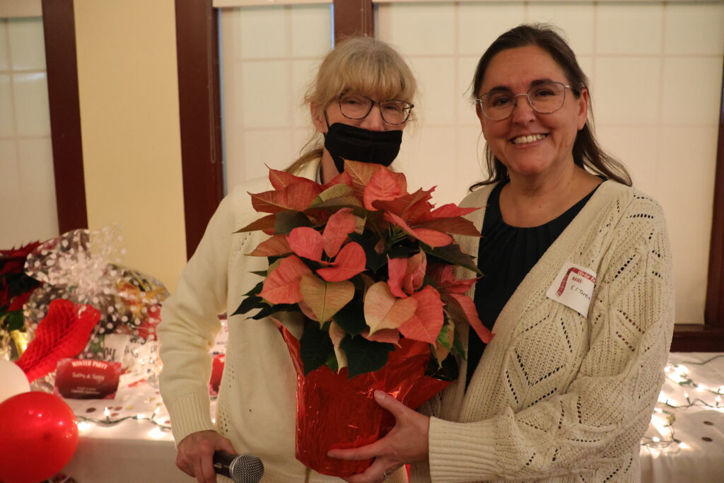 Esther Kruse wins a poinsettia, and is given it by Vicki McCracken at the Winter Party in front of the raffles table.