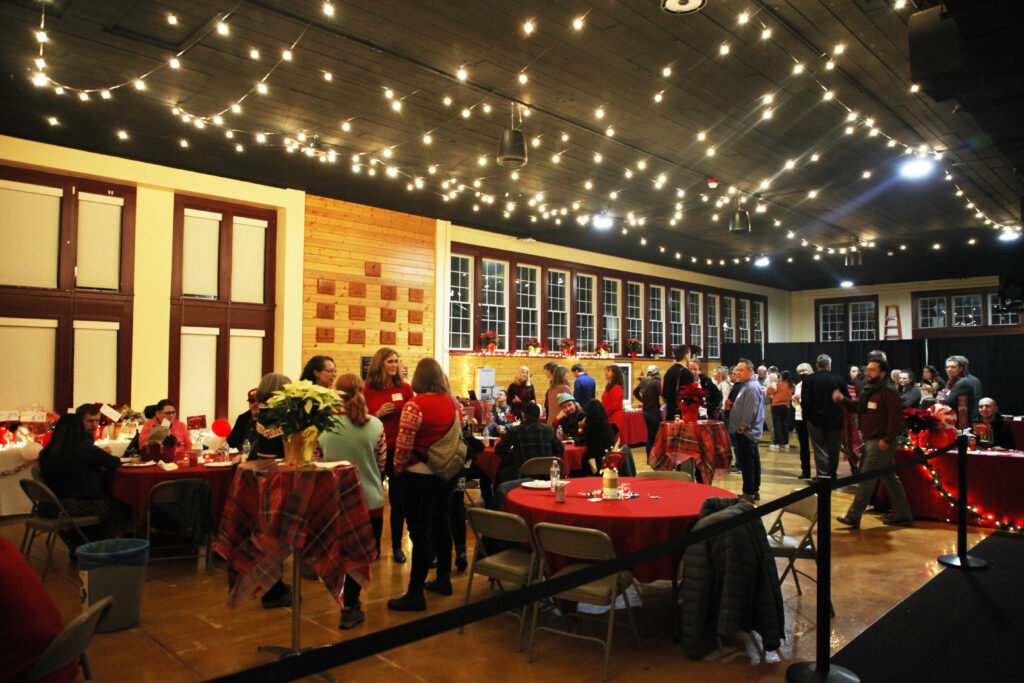 Ensminger Pavilion is full of sparkling lights, attendees in holiday sweaters, red plaid and bright red tablecloths, and many smiling faces.